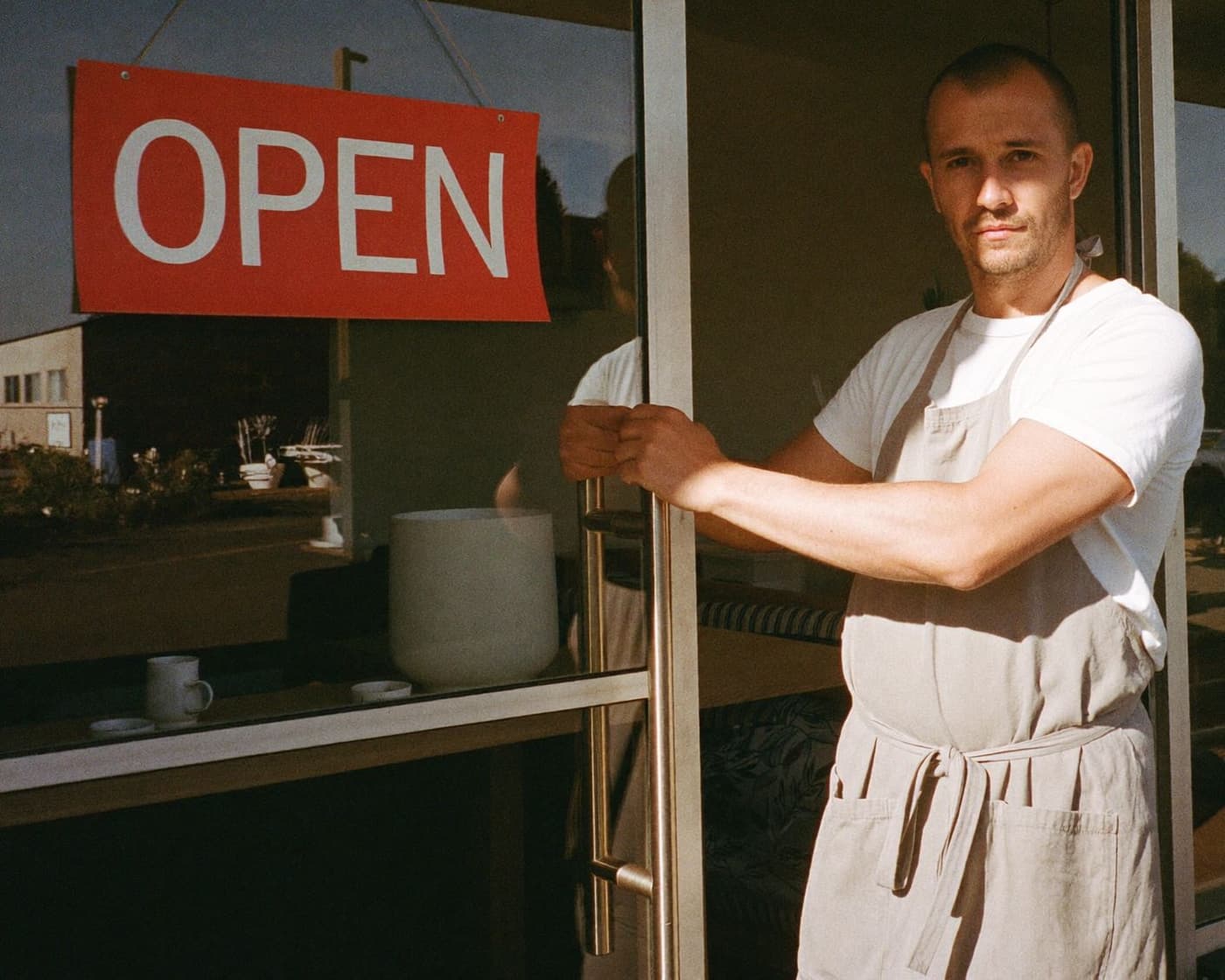 A cafe owner standing at the front door of his shop with the open sign up